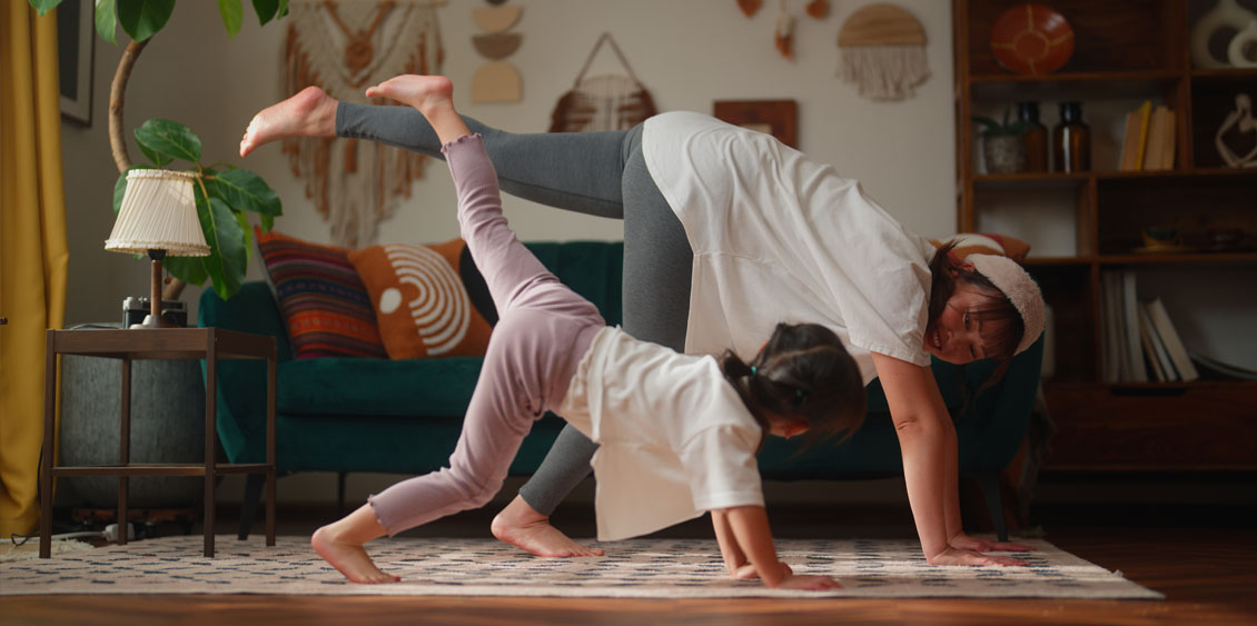 Mother and her small daughter practicing yoga in the living room at home