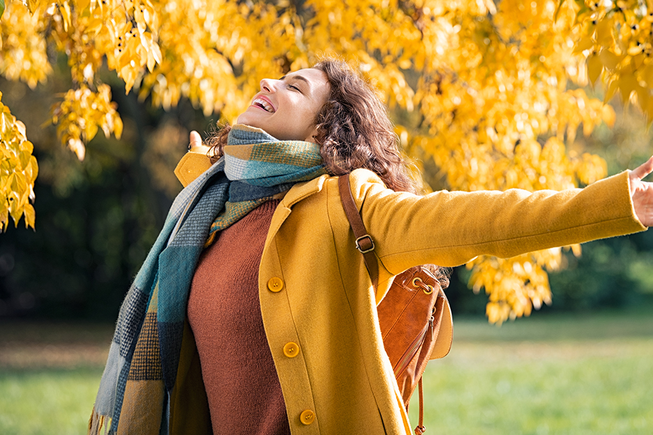 Woman opening her arms under a tree with autumn colors