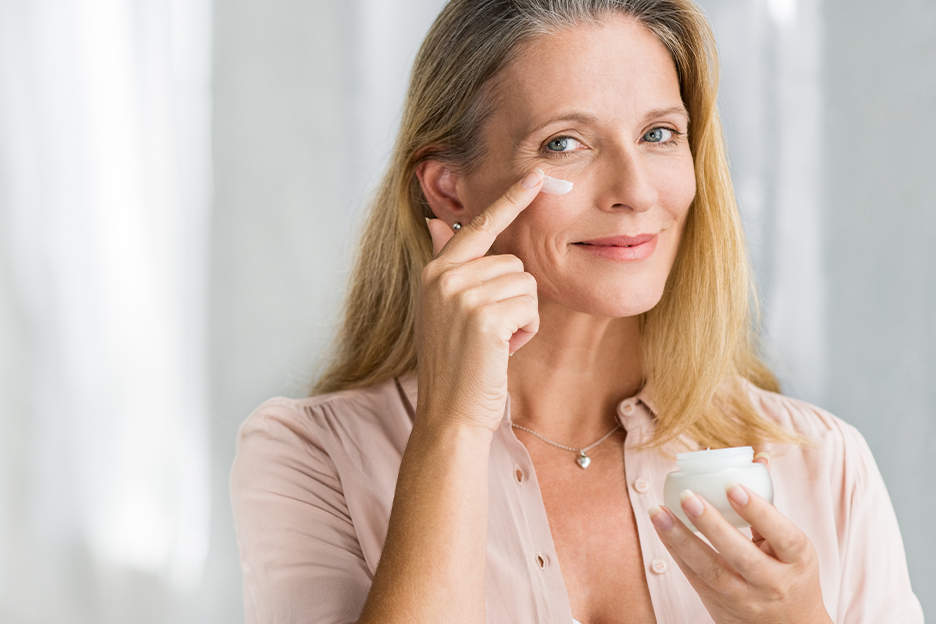 A woman applies cream fos mature skin under her eye.