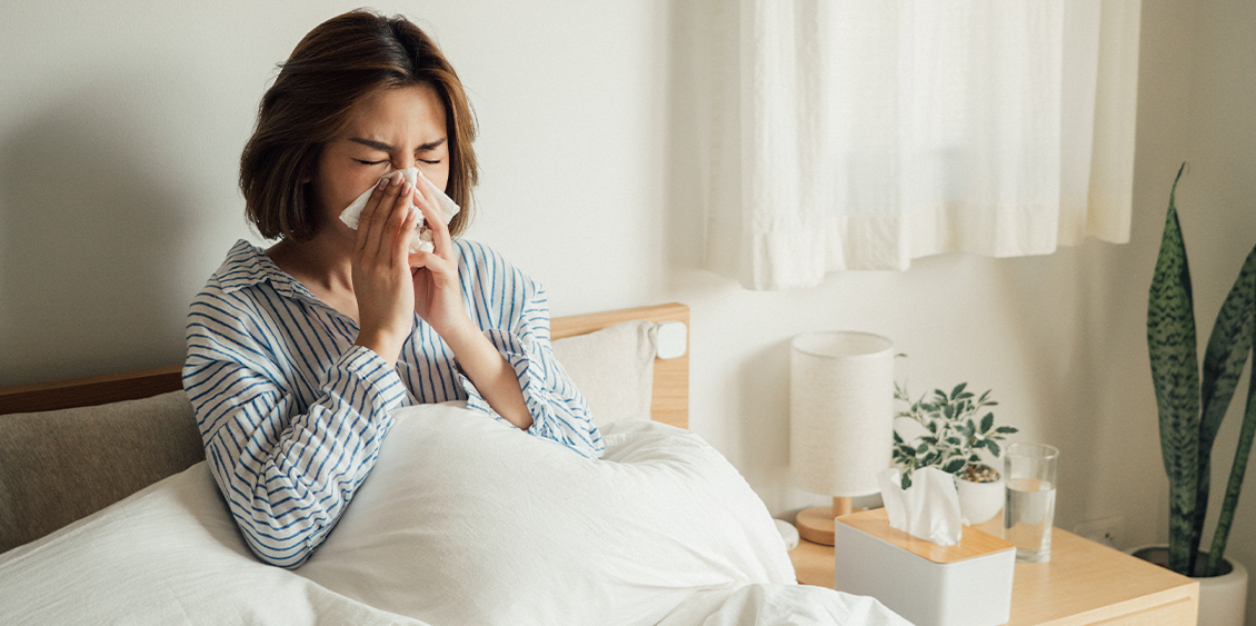 Une femme, allongée dans son lit, a attrapé un rhume et se mouche