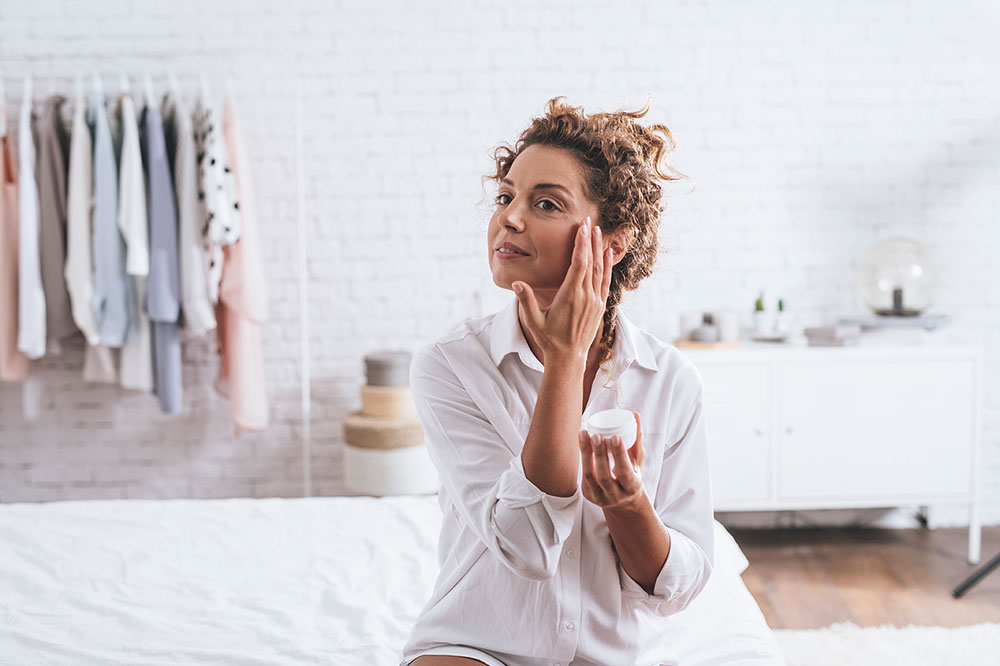 Woman applying cream on her face during her beauty routine.