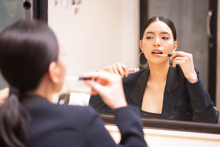 A woman applies cream lipstick in front of a mirror