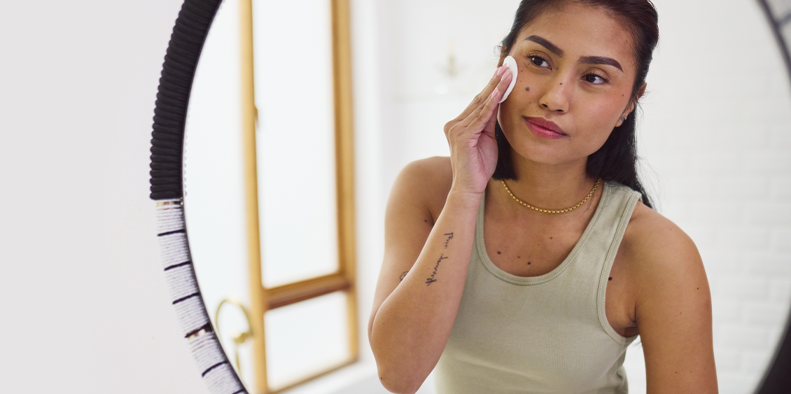 An Asian woman looks in the mirror while using an exfoliating pad on her face.