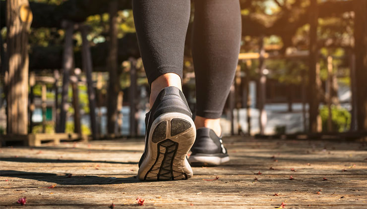 Gros plan sur les jambes d’une femme vêtue de leggings et de souliers de sport noirs, qui marche dans un parc ensoleillé.
