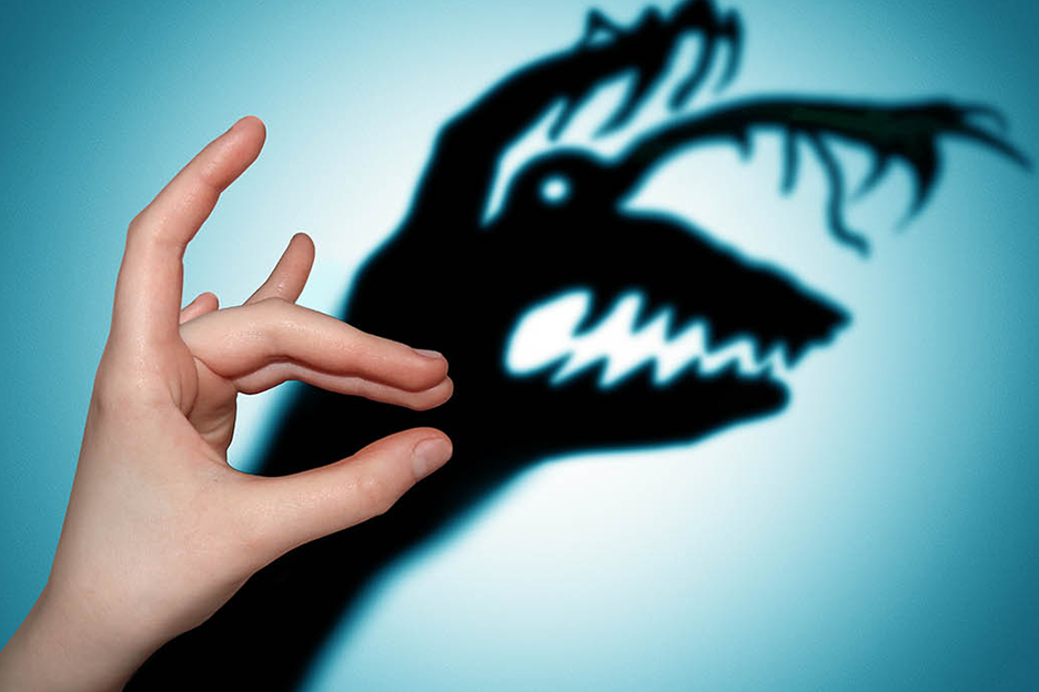 A child’s or teenager’s hand casts a shadow of a monster onto a blue wall to represent mental illness among young people.