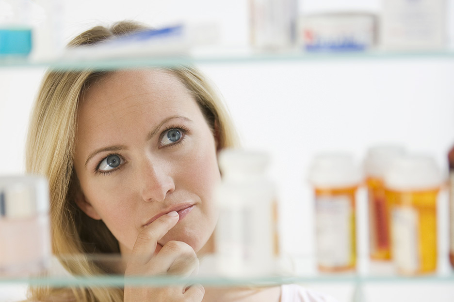 Une femme s'interroge devant le contenu de sa pharmacie.