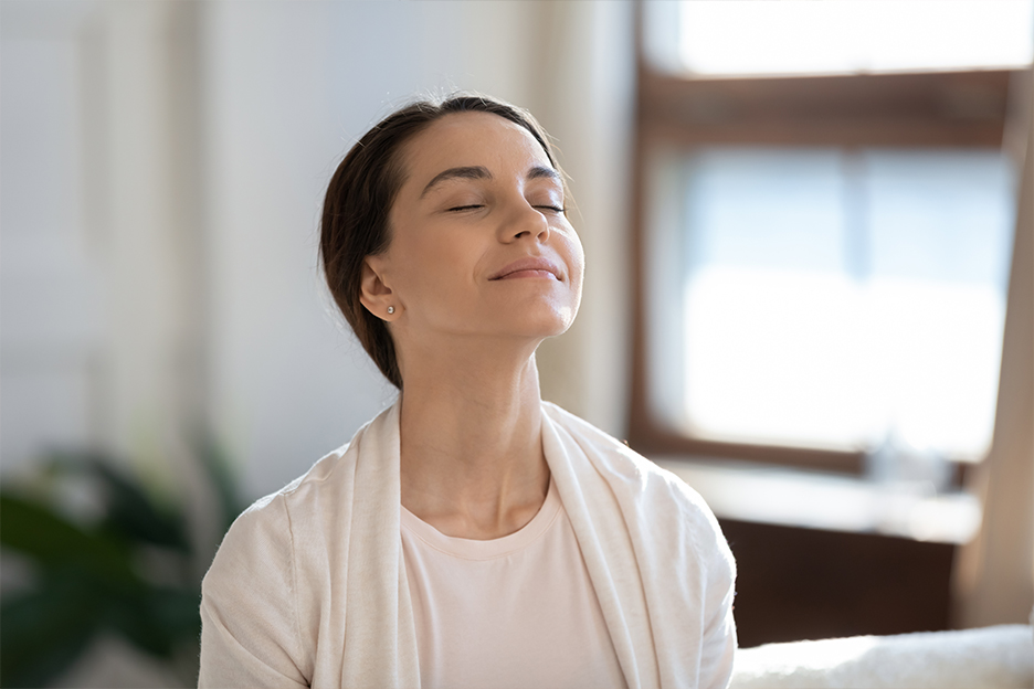 Woman with closed eyes in a room bathed in natural sunlight, illustrating the benefits of light therapy.