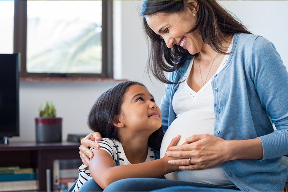 A young girl touches her healthy, pregnant mother's belly. 