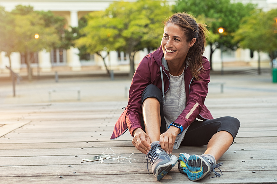 A young woman in running clothes ties her shoes before training outside to prepare for a sporting event. 