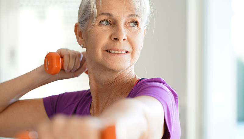 A woman in her sixties does fitness exercises with weights in her hands.
