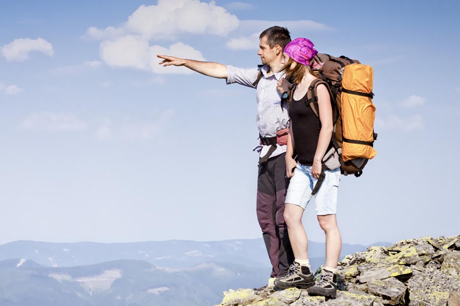 A couple on a trip is contemplating the horizon on top of a mountain.